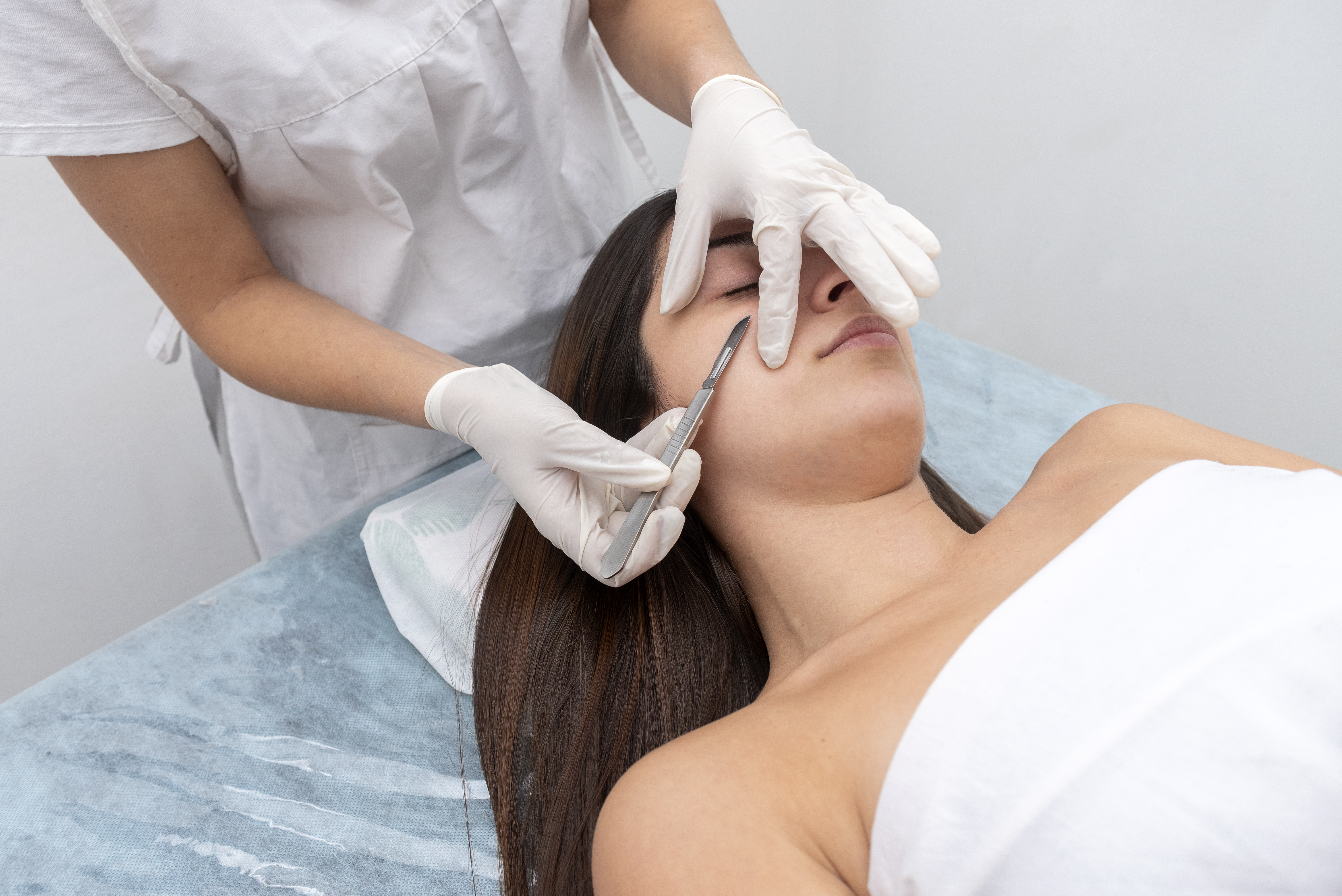 Closeup of the doctor with a scalpel treating the woman's skin. Dermaplaning treatment.